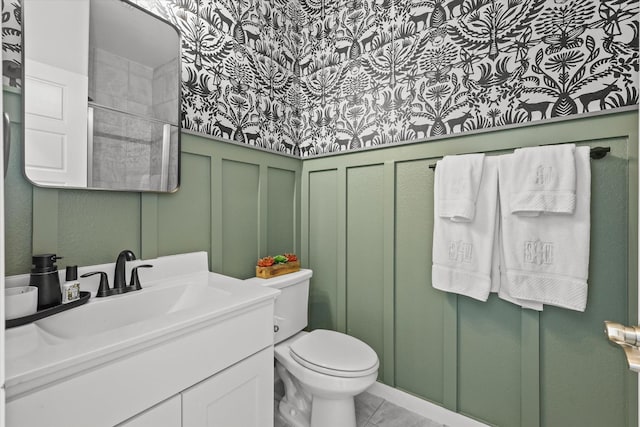 bathroom featuring a wainscoted wall, a decorative wall, toilet, vanity, and tile patterned floors