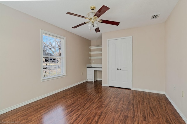 unfurnished bedroom featuring dark wood finished floors, built in desk, a closet, visible vents, and baseboards