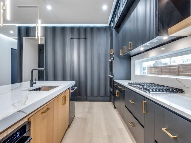 kitchen with light stone counters, light wood-style floors, stainless steel gas stovetop, and a sink