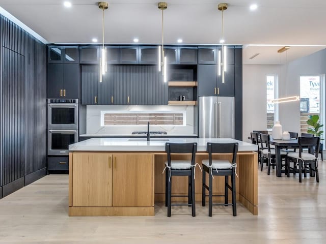 kitchen featuring a sink, light countertops, appliances with stainless steel finishes, light wood finished floors, and an island with sink