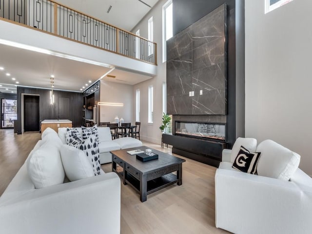 living room with a towering ceiling, light wood-style floors, and a premium fireplace