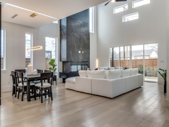 living area with a towering ceiling, a premium fireplace, wood finished floors, and visible vents