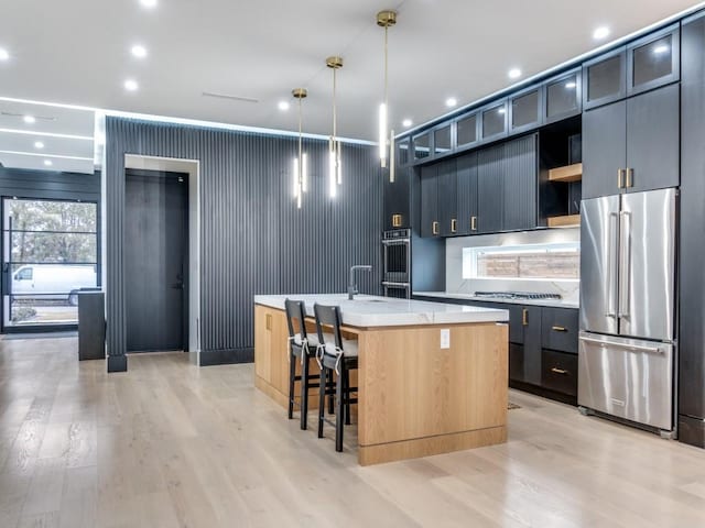 kitchen with light wood finished floors, a center island with sink, appliances with stainless steel finishes, light countertops, and open shelves