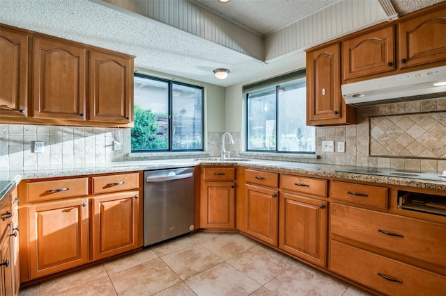 kitchen with a textured ceiling, under cabinet range hood, a sink, stainless steel dishwasher, and brown cabinets