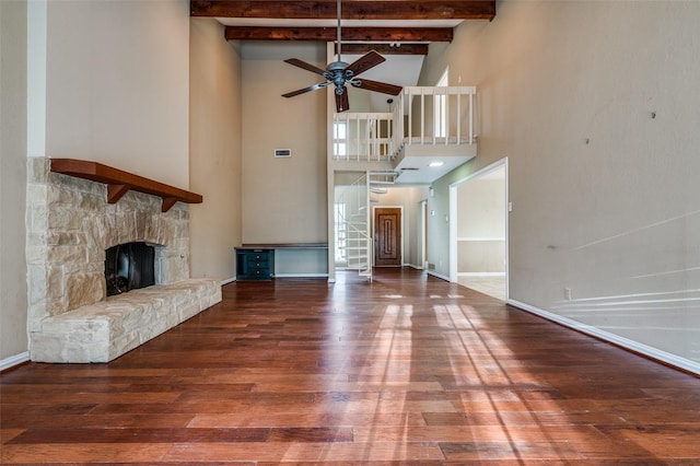 unfurnished living room featuring baseboards, a ceiling fan, wood finished floors, a stone fireplace, and beam ceiling