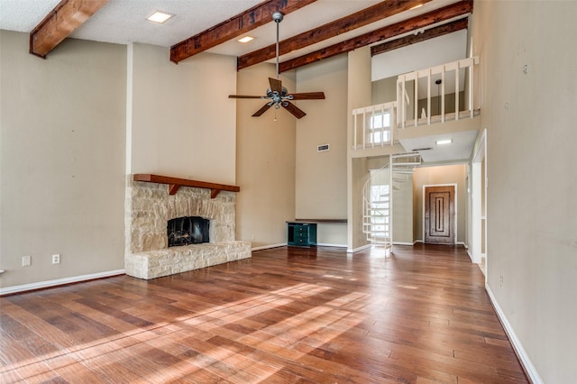 unfurnished living room with ceiling fan, a fireplace, baseboards, hardwood / wood-style floors, and beamed ceiling