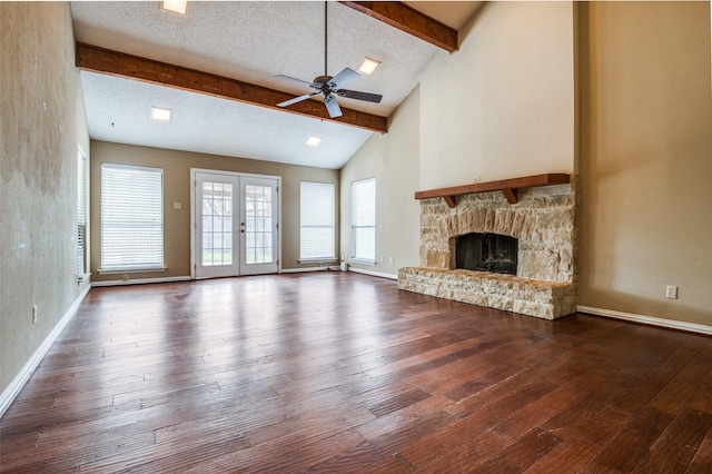 unfurnished living room featuring a textured ceiling, a stone fireplace, french doors, beam ceiling, and hardwood / wood-style floors