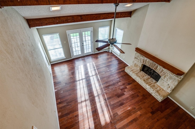 unfurnished living room with french doors, wood finished floors, beamed ceiling, a textured ceiling, and a stone fireplace