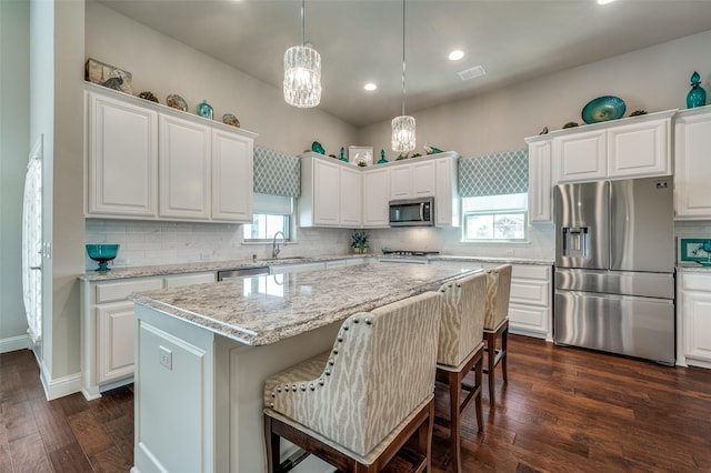 kitchen with stainless steel appliances, backsplash, white cabinetry, a sink, and a kitchen island