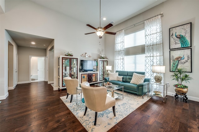 living room with visible vents, a towering ceiling, hardwood / wood-style floors, a ceiling fan, and baseboards