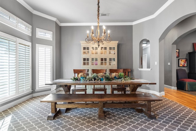 dining space featuring crown molding, a notable chandelier, visible vents, wood finished floors, and baseboards