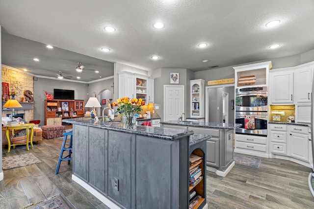 kitchen with open shelves, stainless steel appliances, white cabinetry, wood finished floors, and a kitchen breakfast bar