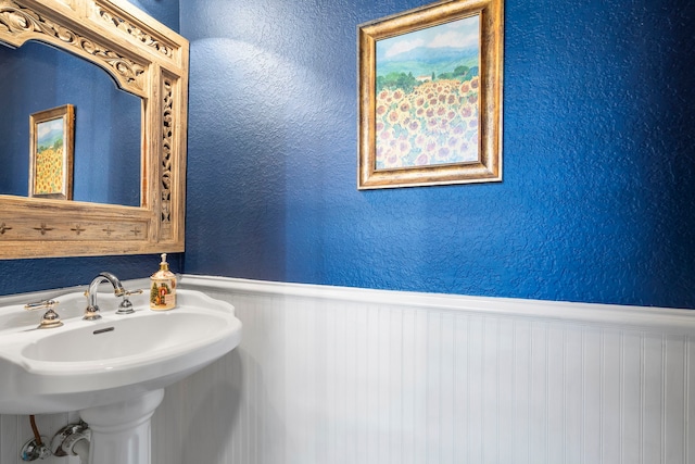 bathroom with wainscoting, a sink, and a textured wall