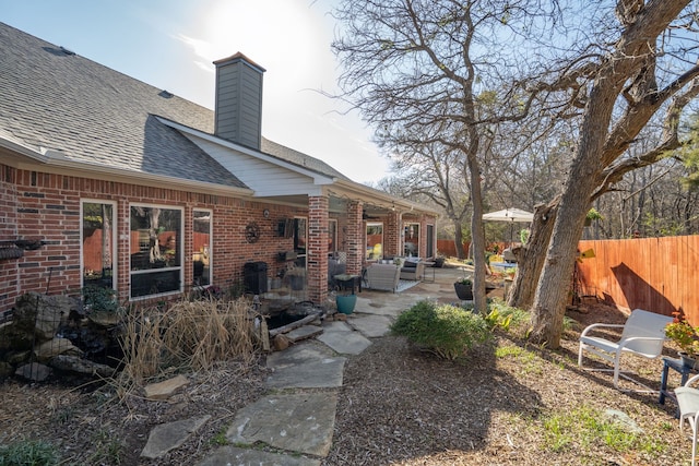 back of house with brick siding, roof with shingles, a patio area, and fence