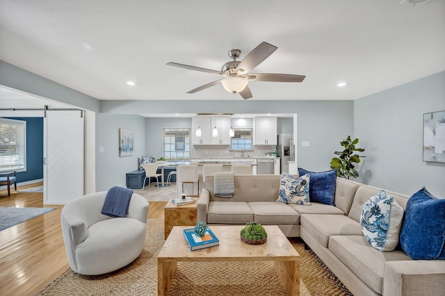 living area with recessed lighting, light wood-style flooring, a barn door, a ceiling fan, and baseboards