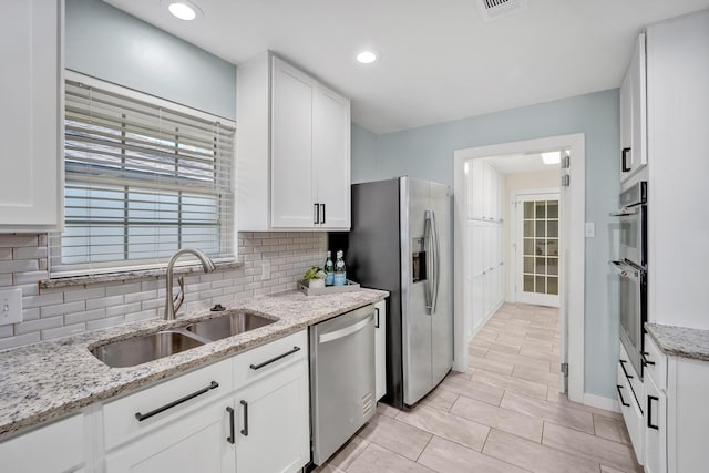 kitchen featuring light stone counters, stainless steel appliances, a sink, white cabinets, and backsplash