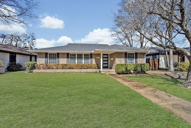 ranch-style house featuring a shingled roof, a front yard, and brick siding