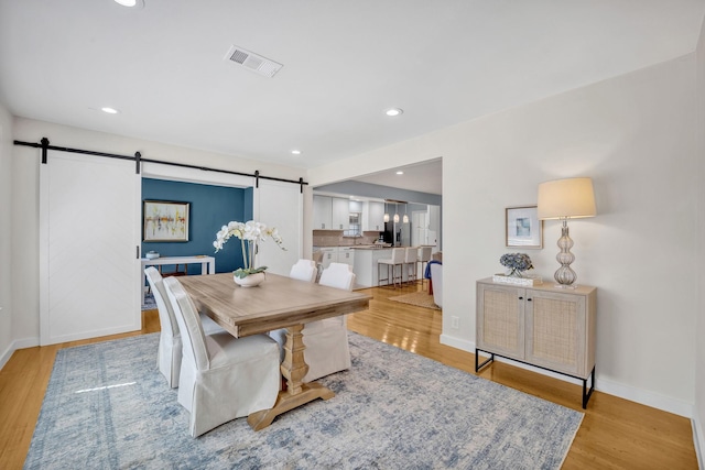 dining room with light wood finished floors, recessed lighting, visible vents, a barn door, and baseboards