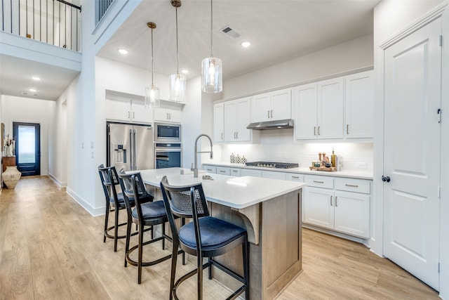 kitchen featuring under cabinet range hood, light countertops, appliances with stainless steel finishes, light wood-type flooring, and decorative backsplash