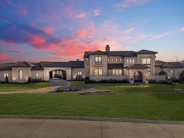 mediterranean / spanish-style house featuring concrete driveway, a tiled roof, a lawn, stucco siding, and a chimney