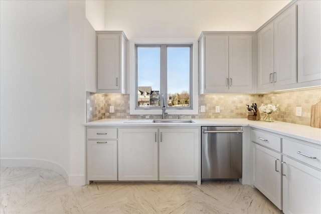 kitchen with baseboards, decorative backsplash, light countertops, stainless steel dishwasher, and a sink