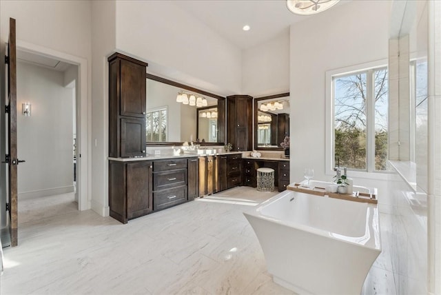 full bathroom with a healthy amount of sunlight, marble finish floor, a freestanding bath, and vanity