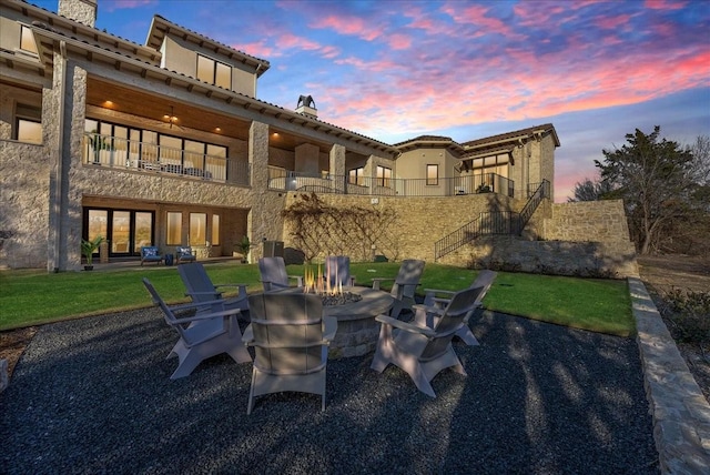 back of property featuring a balcony, a patio area, an outdoor fire pit, and a chimney