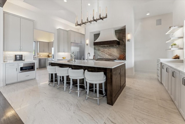 kitchen featuring marble finish floor, appliances with stainless steel finishes, a kitchen island with sink, and custom range hood