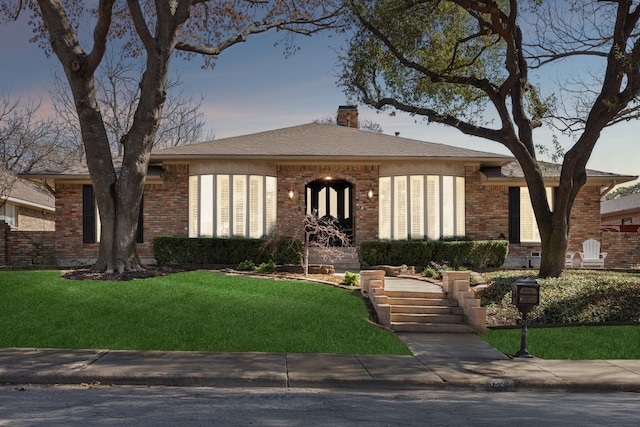 view of front of property featuring a front yard, brick siding, a chimney, and roof with shingles