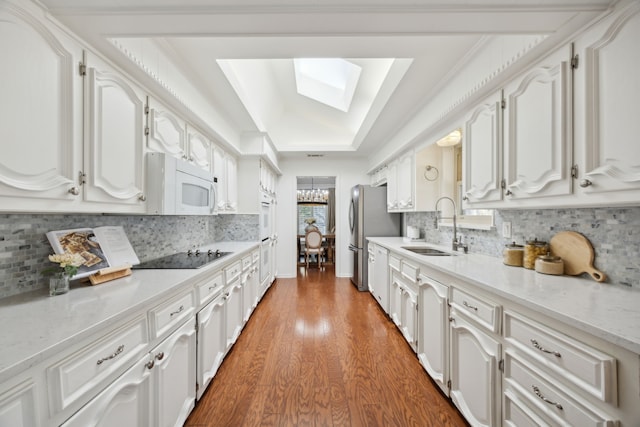 kitchen with a skylight, a tray ceiling, white microwave, a sink, and black electric cooktop