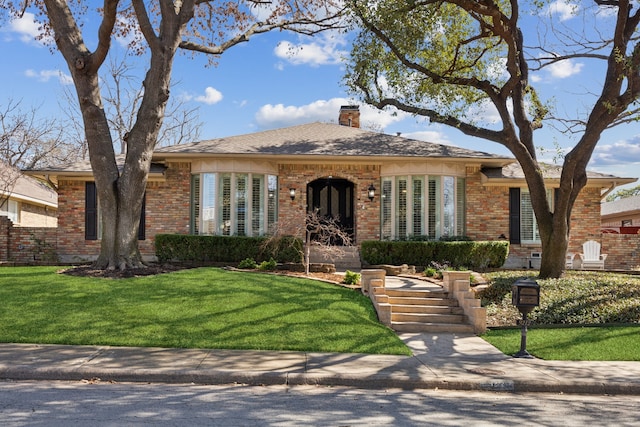 ranch-style house featuring a front yard, a chimney, and brick siding