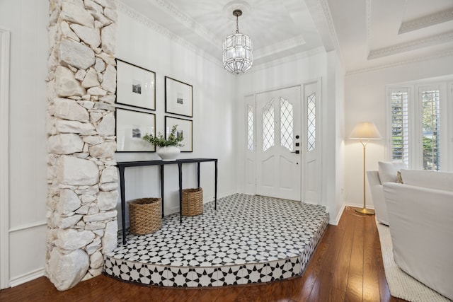 entryway with a notable chandelier, wood finished floors, baseboards, a raised ceiling, and crown molding