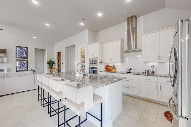 kitchen with visible vents, appliances with stainless steel finishes, open floor plan, light stone countertops, and wall chimney exhaust hood