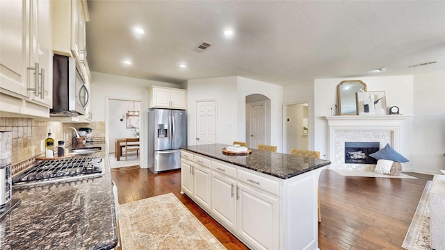 kitchen with dark wood-style flooring, a fireplace, a sink, appliances with stainless steel finishes, and a center island