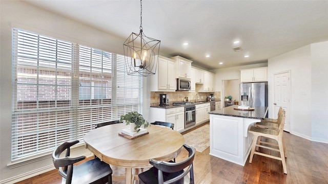 kitchen with decorative backsplash, appliances with stainless steel finishes, a kitchen island, light wood-type flooring, and a kitchen breakfast bar