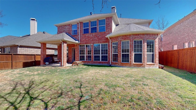 rear view of house featuring a yard, a fenced backyard, and brick siding