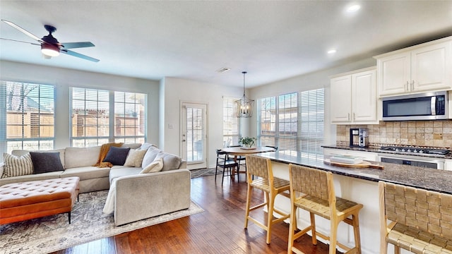 living room with ceiling fan with notable chandelier, dark wood finished floors, visible vents, and a healthy amount of sunlight