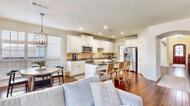 kitchen with arched walkways, dark wood-style flooring, stainless steel appliances, visible vents, and a kitchen bar