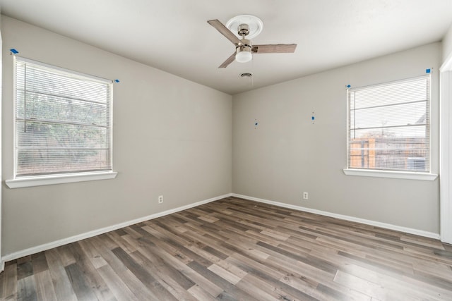 empty room with visible vents, ceiling fan, baseboards, and wood finished floors