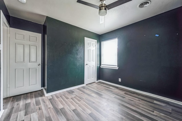 empty room with visible vents, ceiling fan, baseboards, and wood finished floors