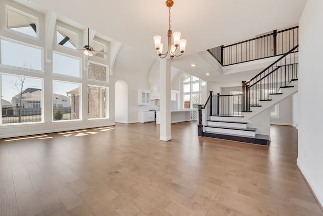 unfurnished living room featuring stairs, ceiling fan with notable chandelier, wood finished floors, and a towering ceiling