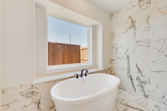 full bathroom with marble finish floor, a freestanding tub, and tile walls