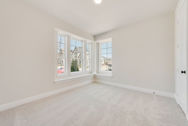 spare room with baseboards and light colored carpet