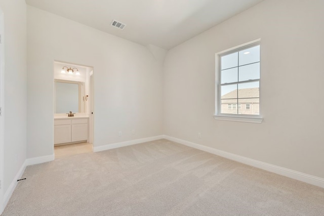 unfurnished bedroom featuring baseboards, visible vents, ensuite bathroom, and light colored carpet