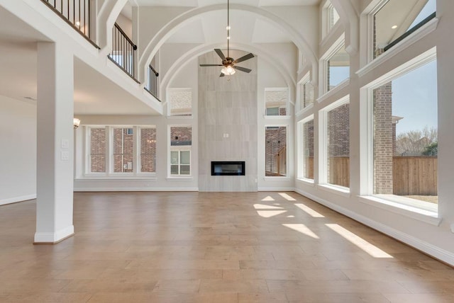 unfurnished living room featuring a wealth of natural light, baseboards, a tiled fireplace, and wood finished floors