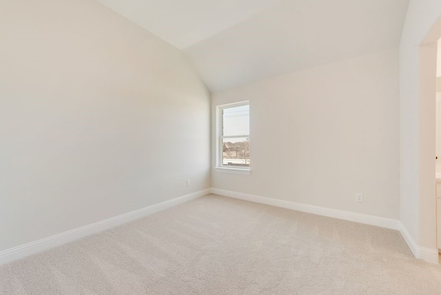 empty room featuring baseboards, vaulted ceiling, and light colored carpet