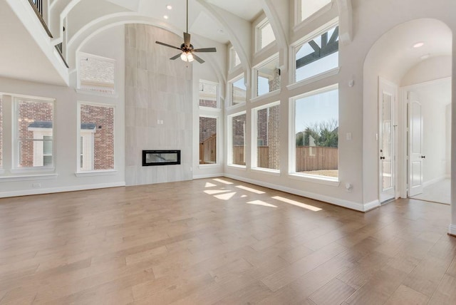 unfurnished living room with a high ceiling, a ceiling fan, wood finished floors, and a tile fireplace