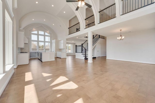 unfurnished living room with ceiling fan with notable chandelier, a high ceiling, baseboards, and stairs