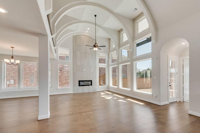 unfurnished living room featuring a high ceiling, ceiling fan with notable chandelier, wood finished floors, and a tile fireplace