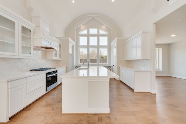 kitchen featuring oven, white cabinetry, light countertops, light wood finished floors, and glass insert cabinets